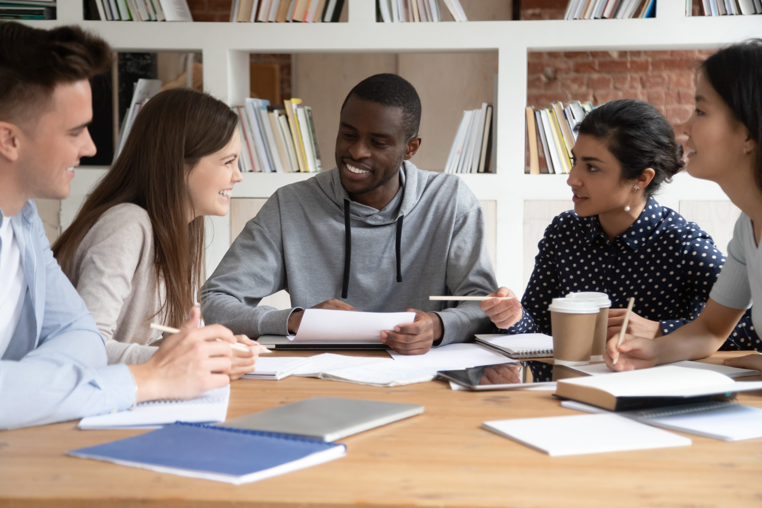 People sitting at a table with notebooks and coffee talking.